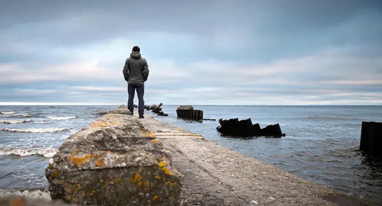 Mand står med ryggen til og ser ud over havet